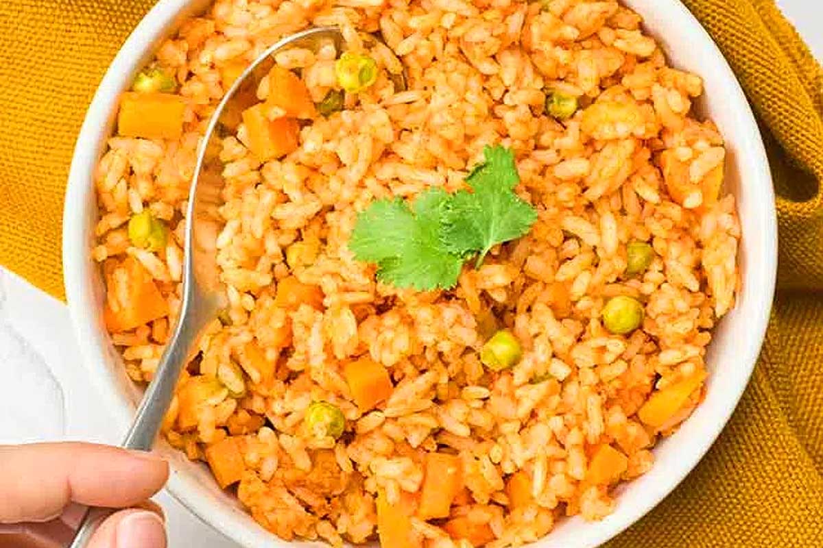 A person holding a bowl of rice with carrots and peas.