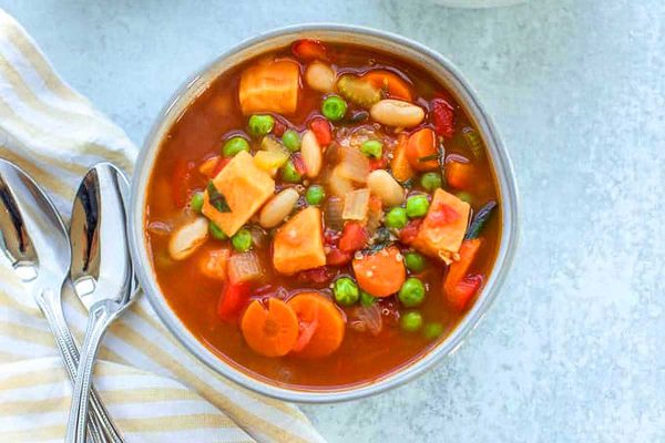 A bowl of soup with carrots, peas and beans.