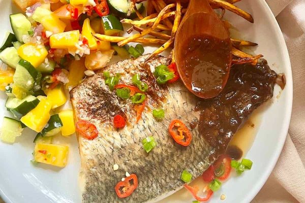 A plate of Asian-inspired fish with fries and sauce on it.