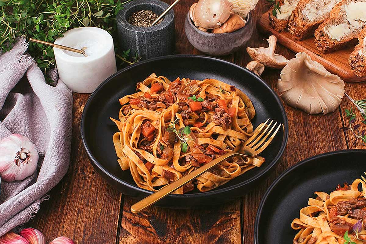 Two bowls of pasta with meat and vegetables on a wooden table.