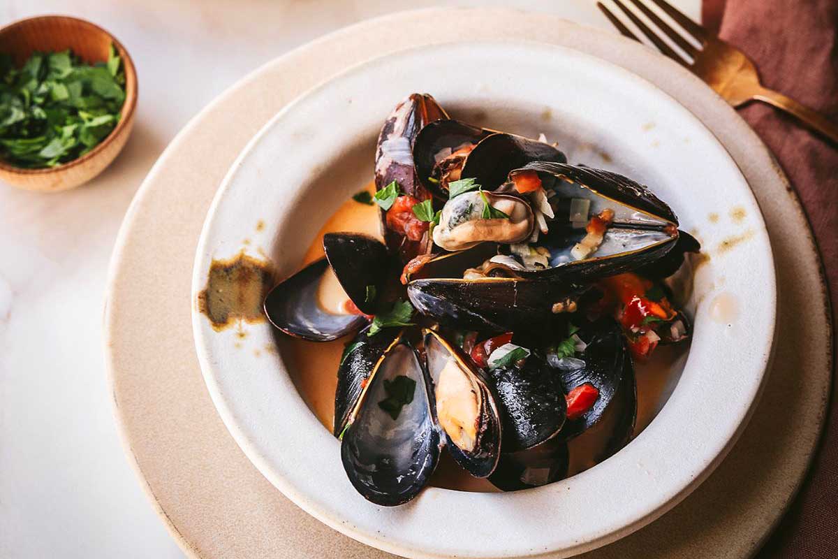 For a romantic date night, savor the exquisite sight of mussels elegantly presented in a pristine white bowl on a beautifully set table.