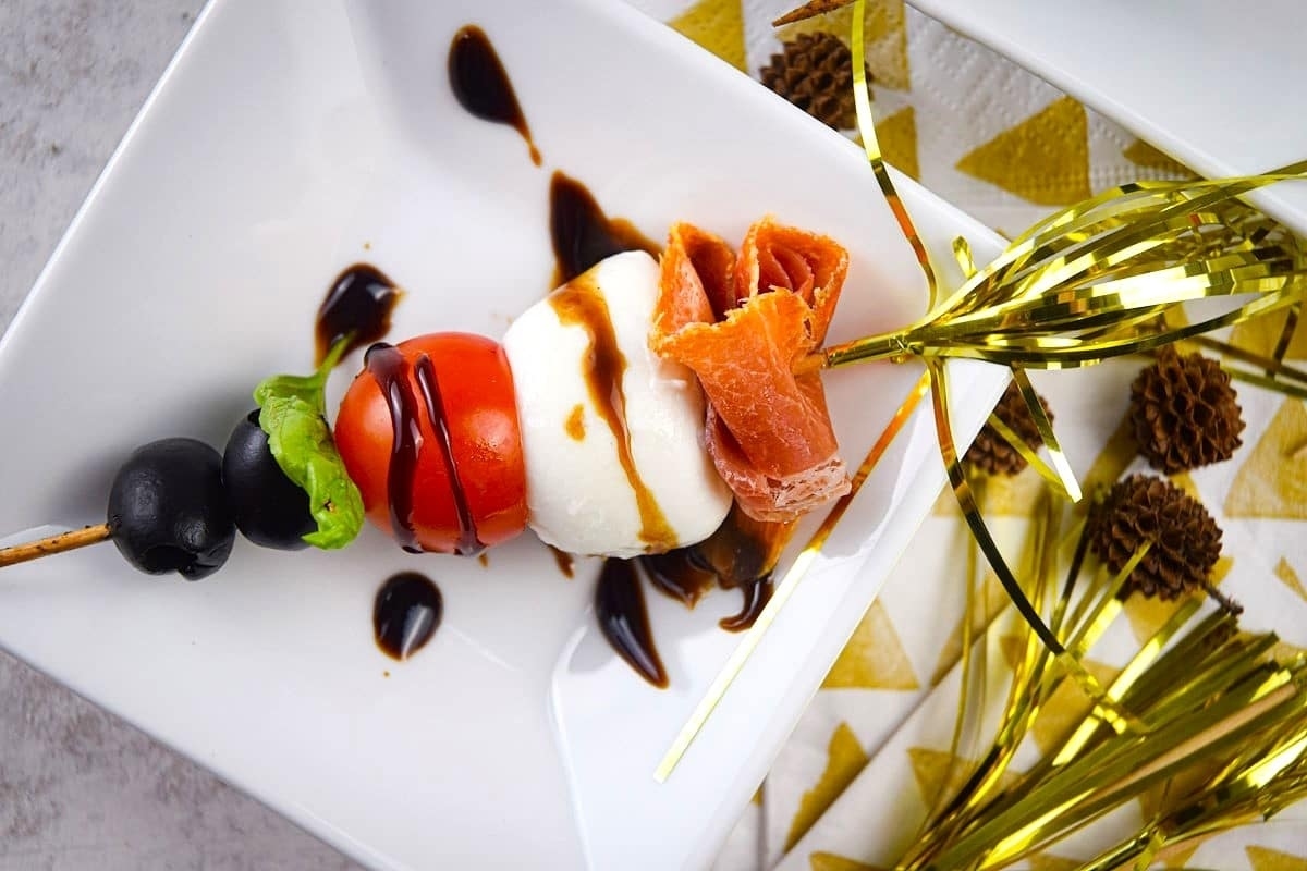 A festive plate of skewers featuring New Year's Eve-inspired appetizers with tomatoes, olives, and salmon.