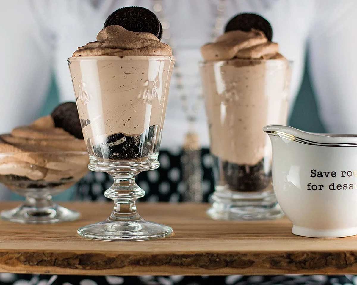 A woman is holding a tray with three Oreo desserts on it.