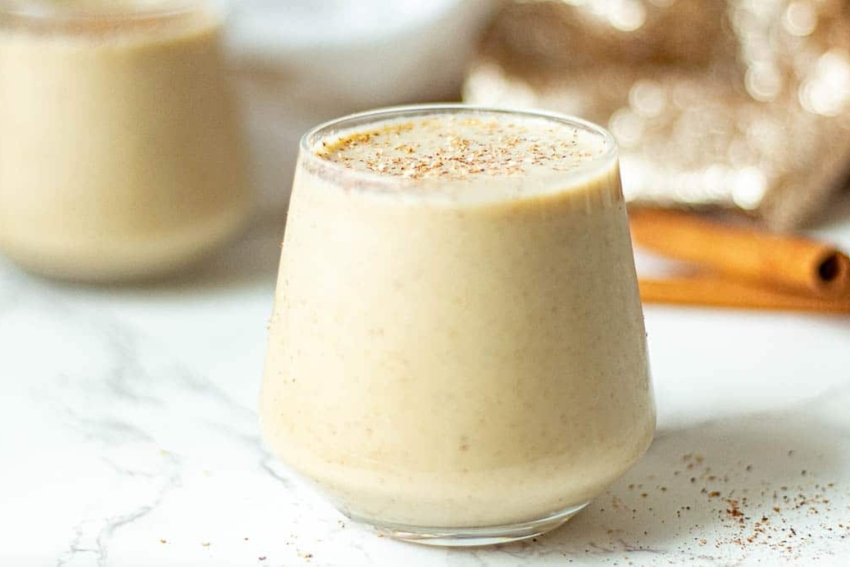 A delicious eggnog smoothie garnished with cinnamon sticks, served on a sleek marble table.