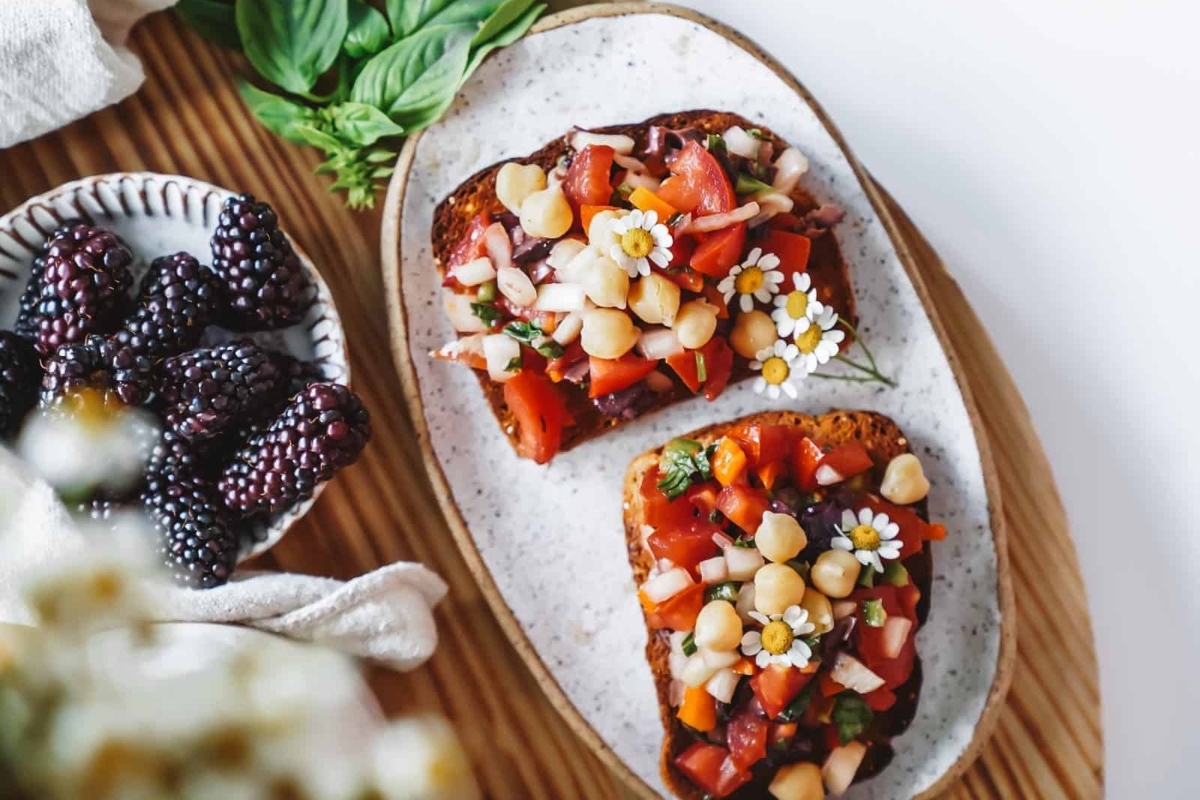 Two slices of bread with blackberries and tomatoes on them.