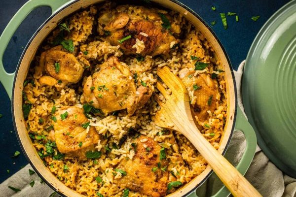 Bone-in chicken breast and rice cooked together in a pan using a wooden spoon.