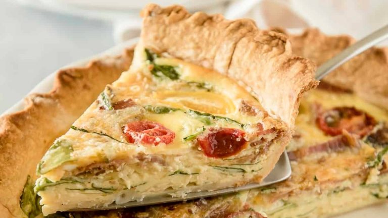 A plate of quiche with tomatoes and spinach.