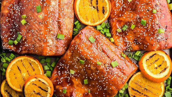 Salmon with orange slices and sesame seeds on a baking sheet.