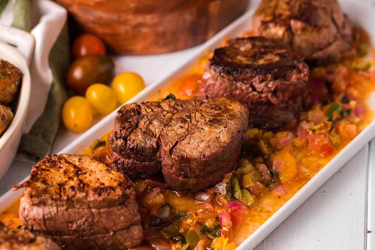 Beef tenderloin with tomato sauce on a white plate.