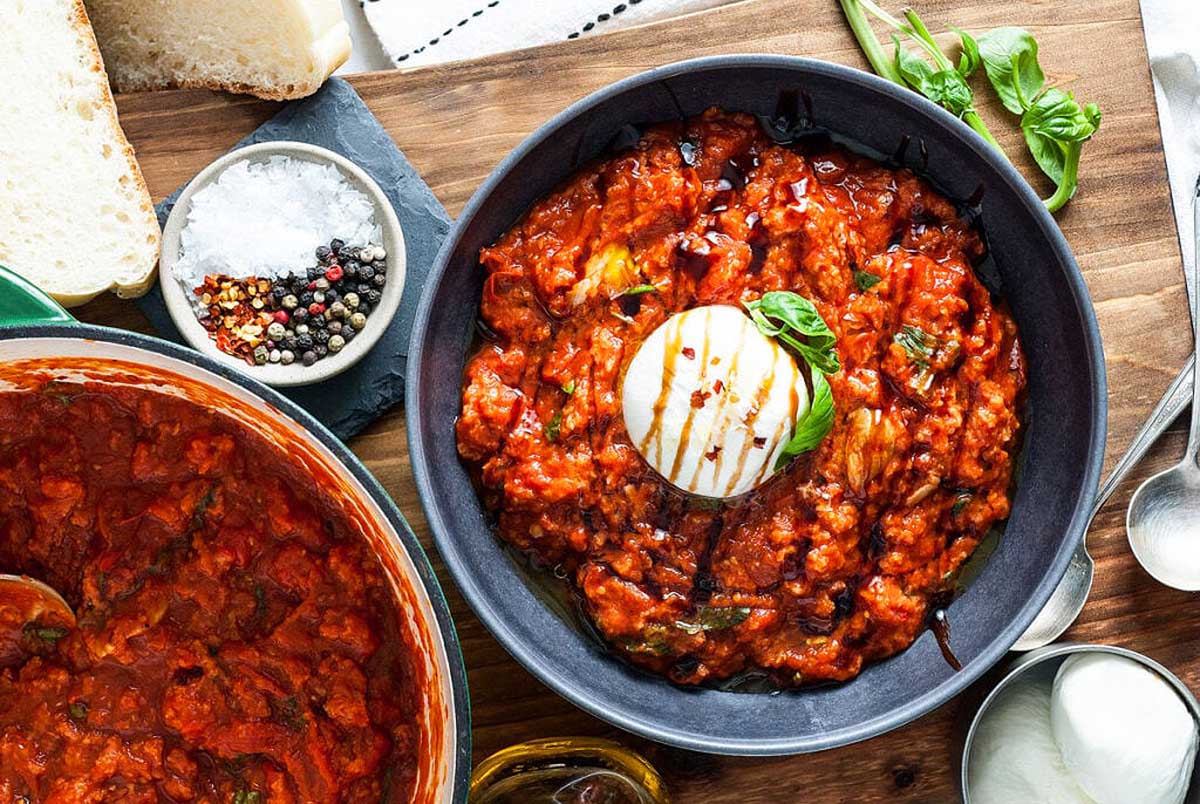 A bowl of tomato sauce and bread on a wooden table.