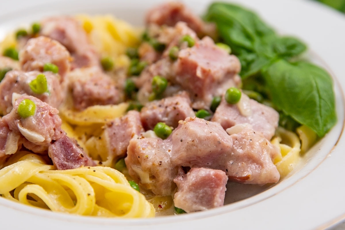 A delightful recipe for pasta with ham and peas served on a white plate, made even more convenient with the use of frozen peas.