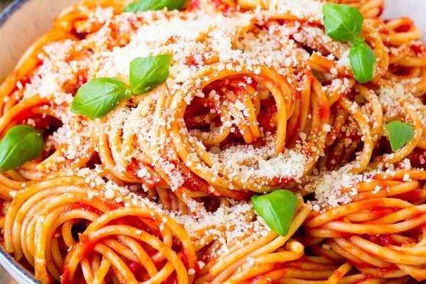 A mouthwatering recipe for spaghetti cooked in a pan, generously topped with parmesan cheese and garnished with fresh basil leaves - surely a delightful way to utilize pantry staples.