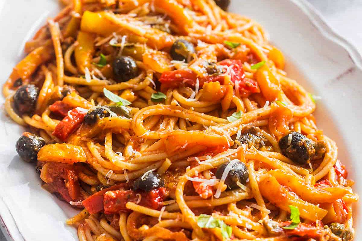 Spaghetti with peppers and olives on a white plate.