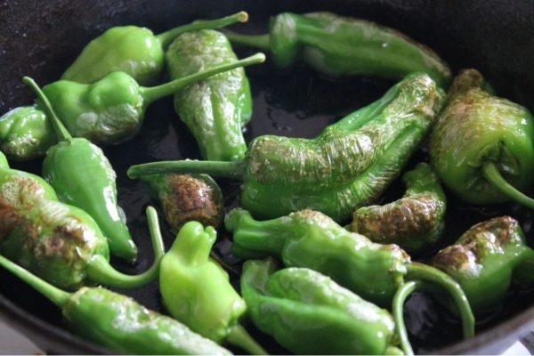 Green peppers being cooked in a frying pan.