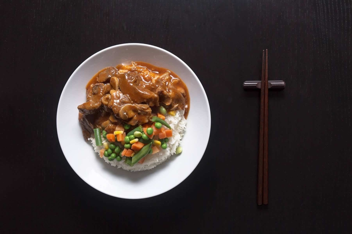 A plate with rice and frozen mixed vegetables on a black background.