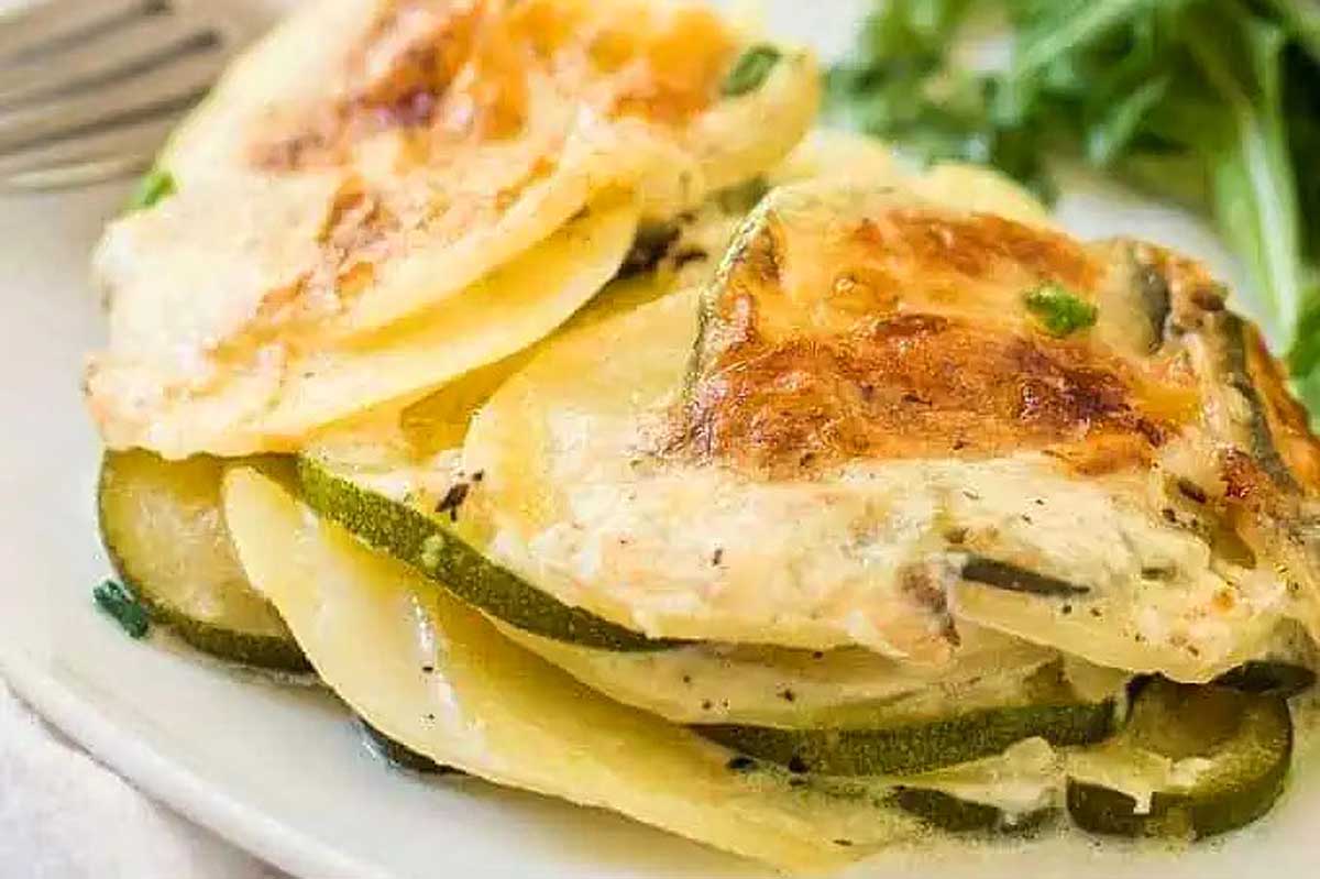 A plate of cheesy zucchini gratin with a fork, featuring zucchini.