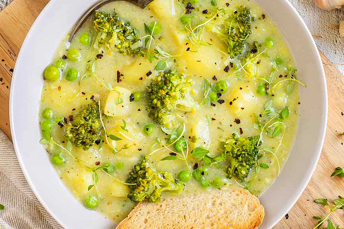A bowl of soup with broccoli, potatoes and peas.