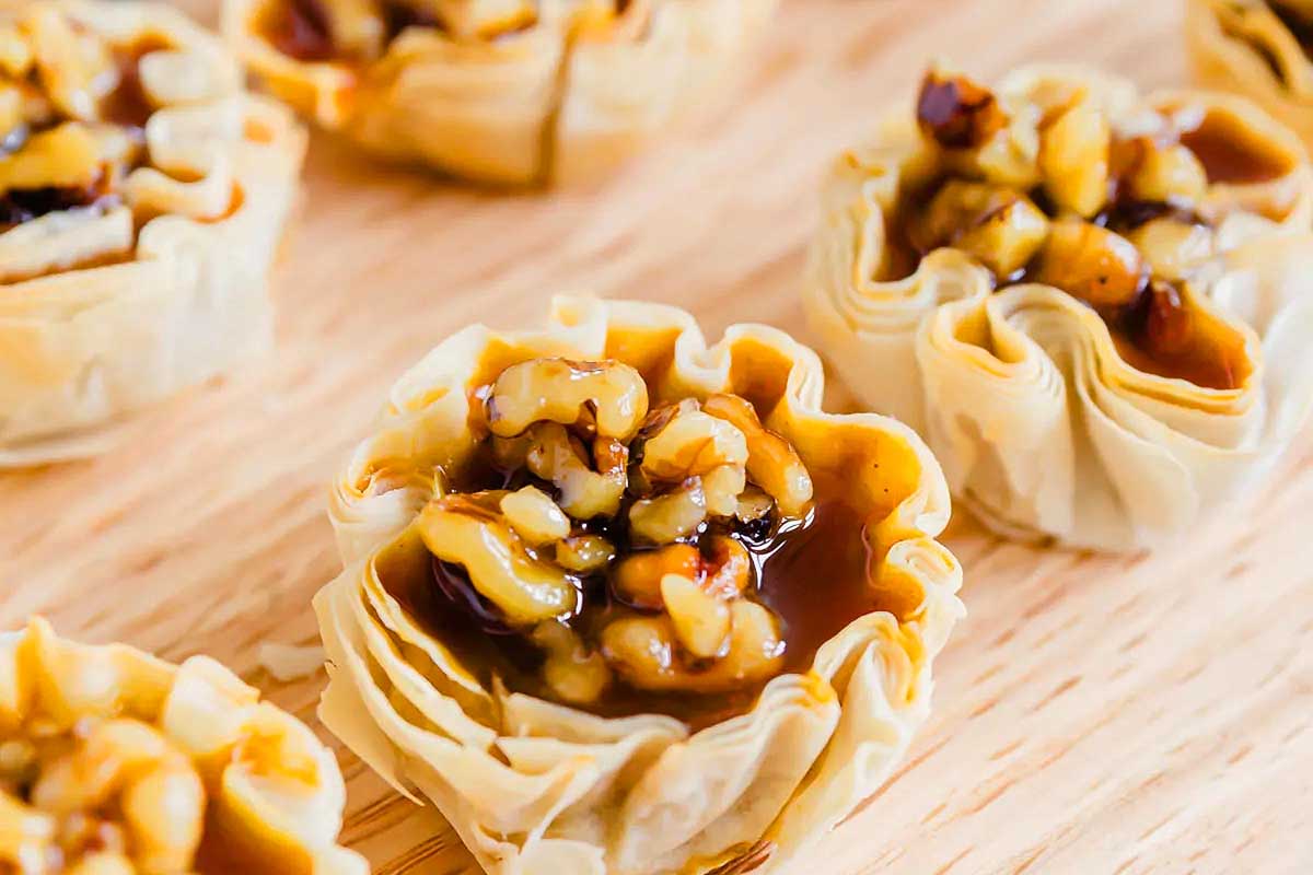 A plate of walnut tarts on a wooden cutting board for Friendsgiving.