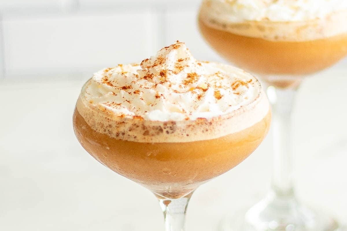 Two Thanksgiving cocktails served in martini glasses, topped with whipped cream and cinnamon.