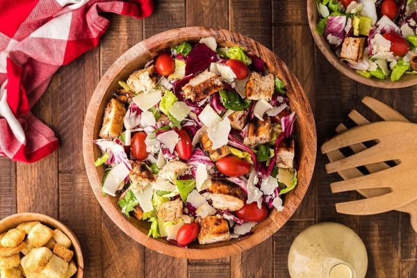 Chicken salad with croutons and tomatoes on a wooden table.