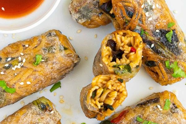 Asian spring rolls with vegetables and sauce on a white plate, perfect for any oriental-inspired meal or appetizer spread.