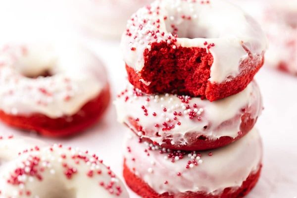 A stack of red velvet donuts with icing and sprinkles.