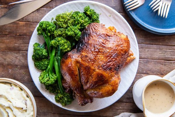 A roast chicken with gravy and broccoli on a plate, perfect for Thanksgiving dinner.