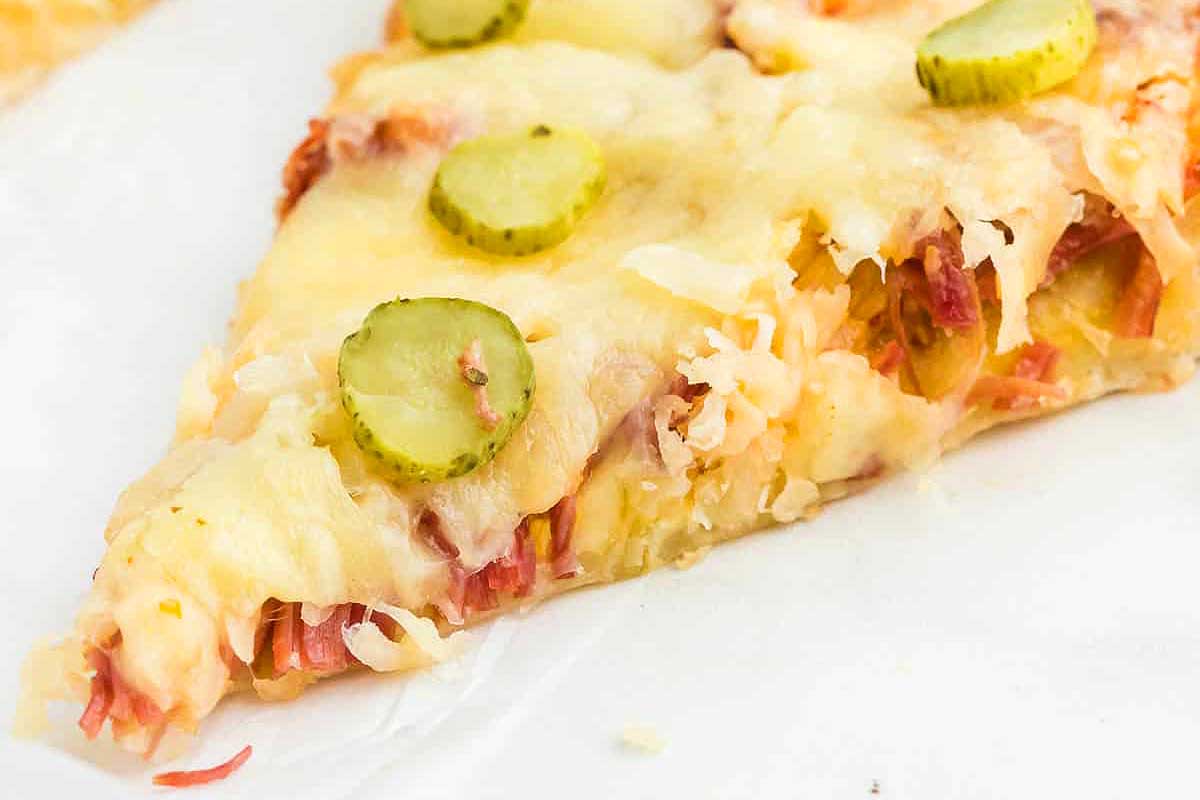 A slice of pizza with cheese and pickles.
