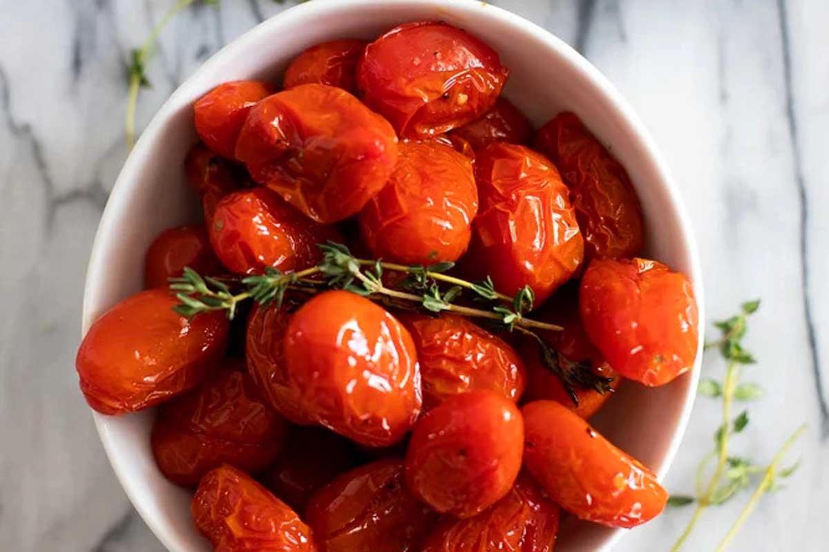 Aromatic roasted tomatoes showcased in a pristine white bowl, garnished elegantly with thyme.