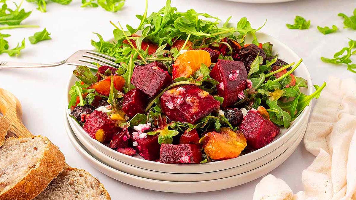 A bowl of beet salad with bread next to it, accompanied by a side of ham.
