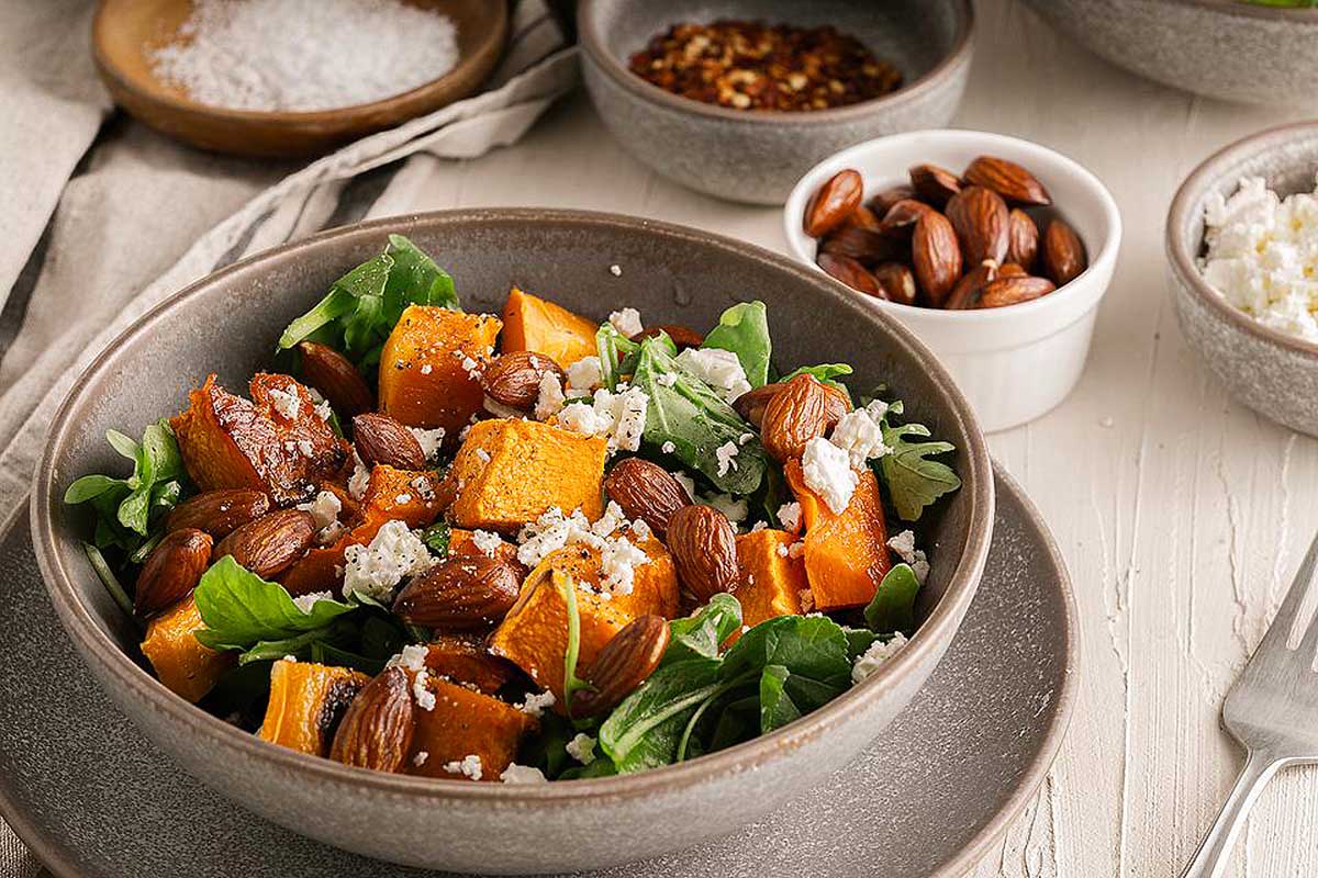 A bowl of sweet potato salad with almonds and spinach.