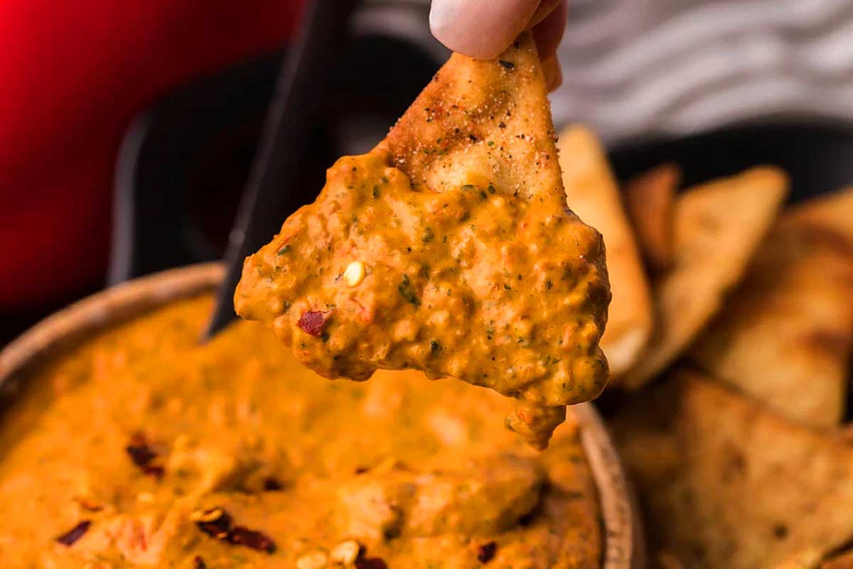 A hand is dipping a tortilla into a bowl of chicken tikka masala dip.