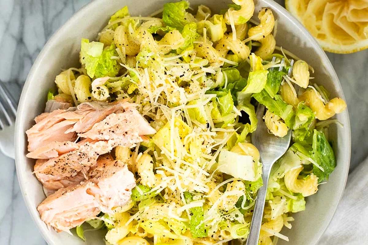 A delicious bowl of pasta salad with fresh salmon and zesty lemon wedges.