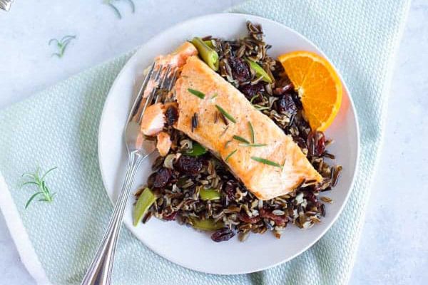Salmon on a plate with rice and orange slices.