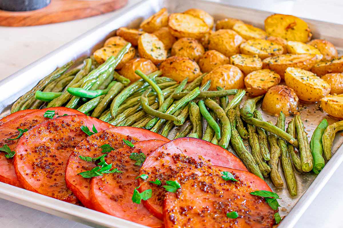A tray of roasted vegetables with green beans and ham steaks.