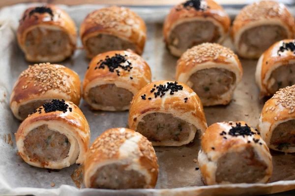 Sausage rolls with sesame seeds on a baking sheet.