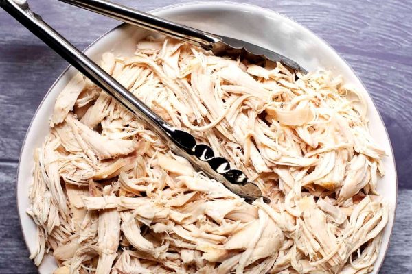 Shredded chicken breast in a white bowl with two forks.