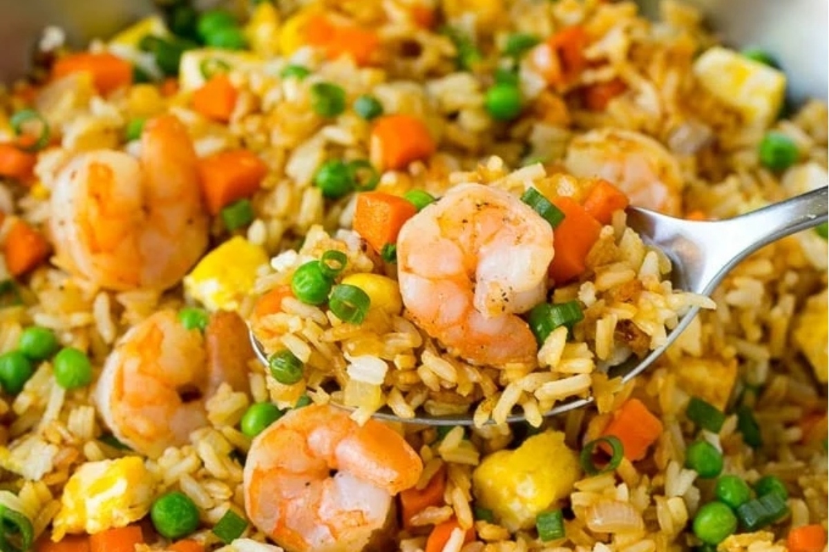A delectable spoonful of fried rice with shrimp, vegetables, and frozen peas.