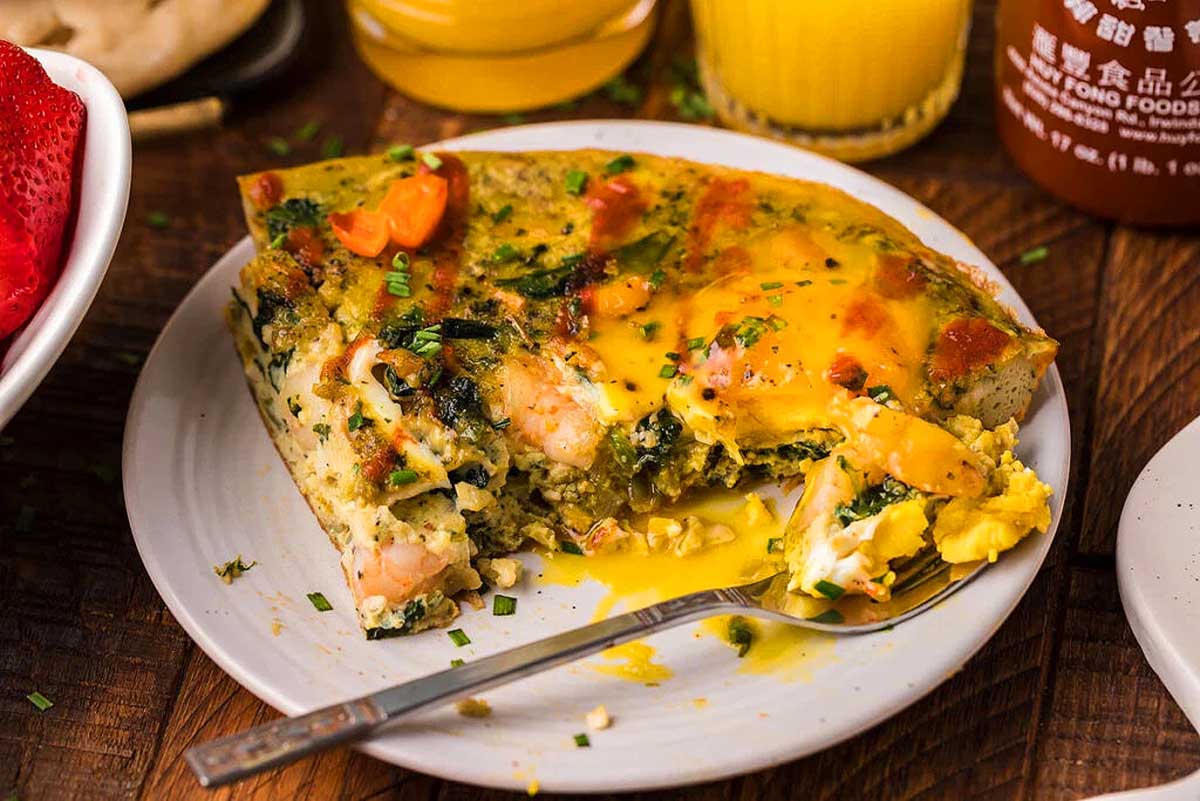 A plate with a slice of quiche and a cup of orange juice.