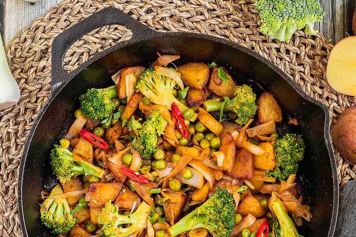 A skillet filled with broccoli, potatoes and peas.