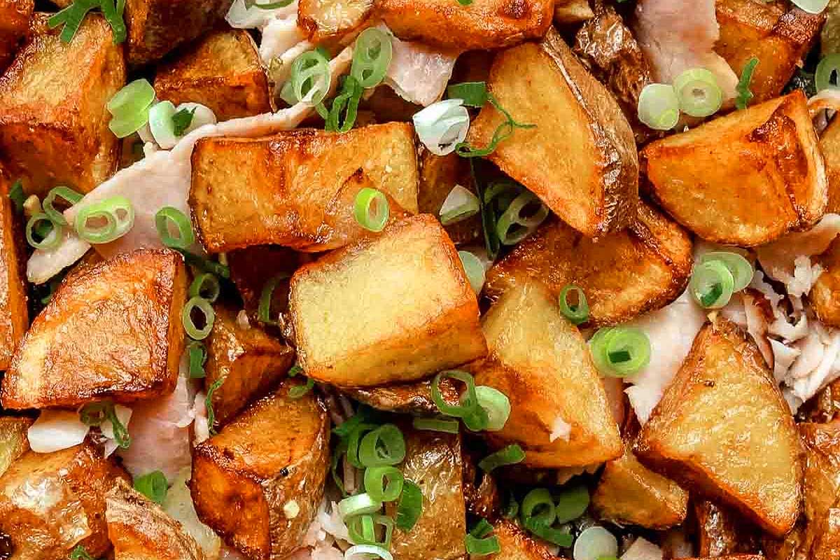 A plate of roasted potatoes with scallions and ham.