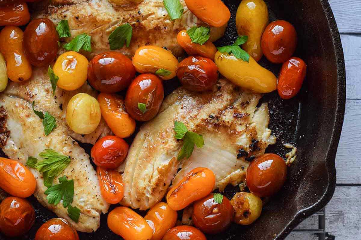 Grilled chicken with tomatoes and herbs in a skillet.