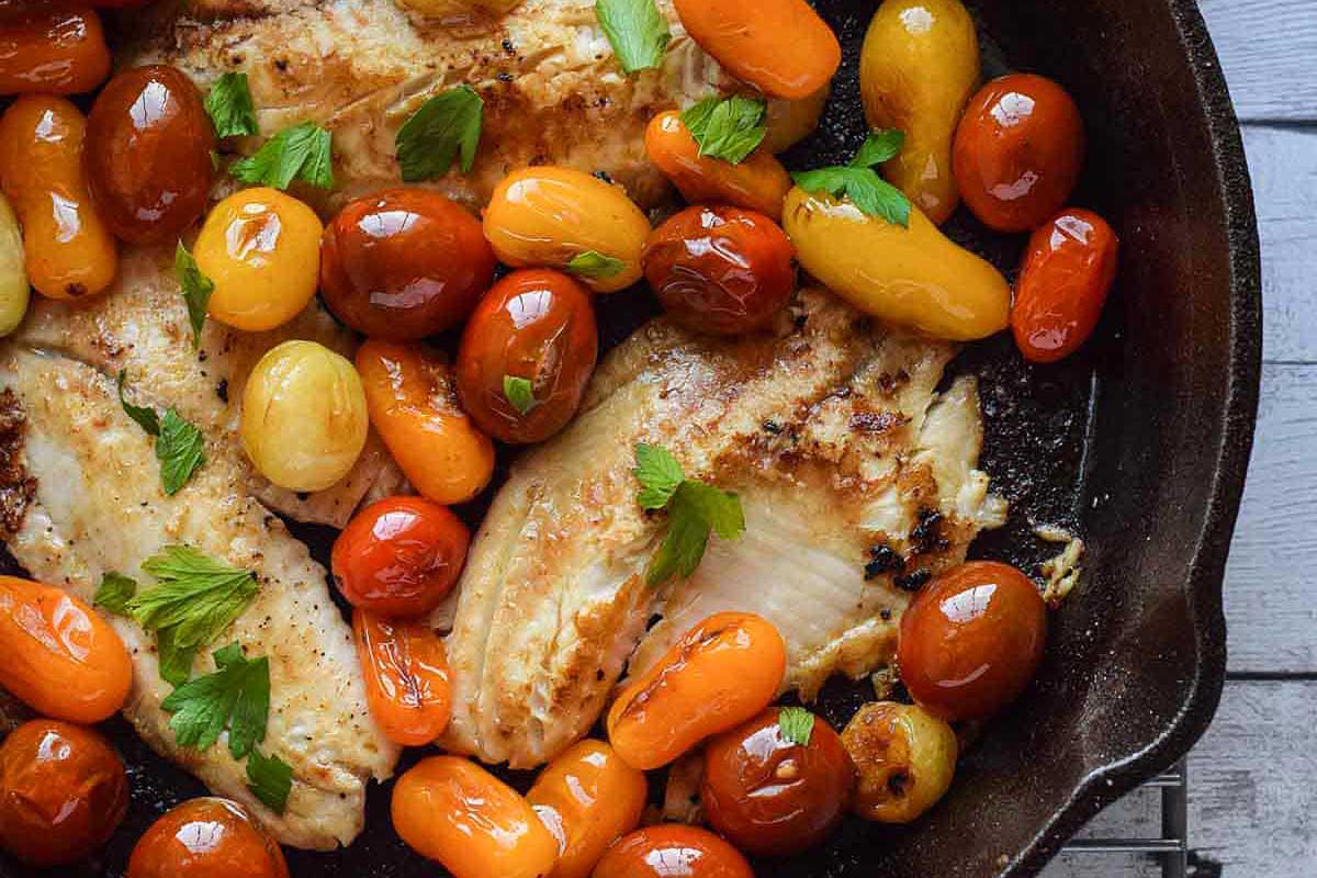 Grilled tilapia with tomatoes and herbs in a skillet.