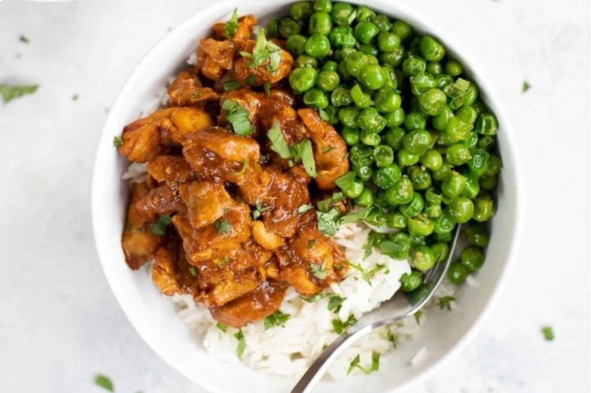 Chicken tikka masala in a white bowl with frozen peas.