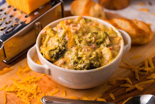 A bowl of broccoli and cheese soup with a cheese grater.