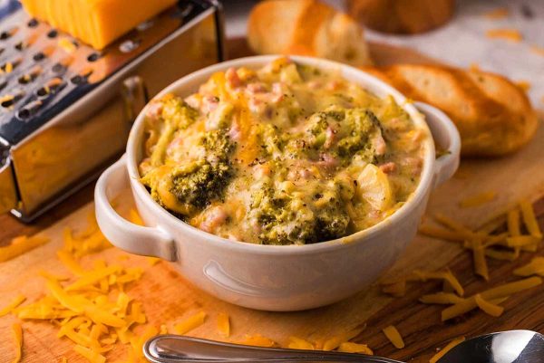 A bowl of Slow Cooker broccoli and cheese Soup on a cutting board.