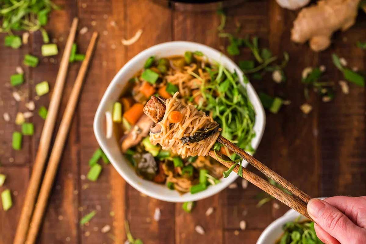 A person holding chopsticks in front of a bowl of noodle soup.