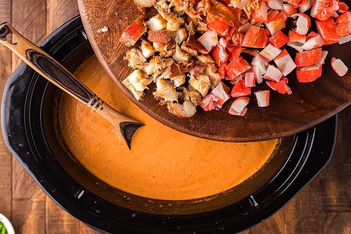 A slow cooker full of clam chowder with a wooden spoon.