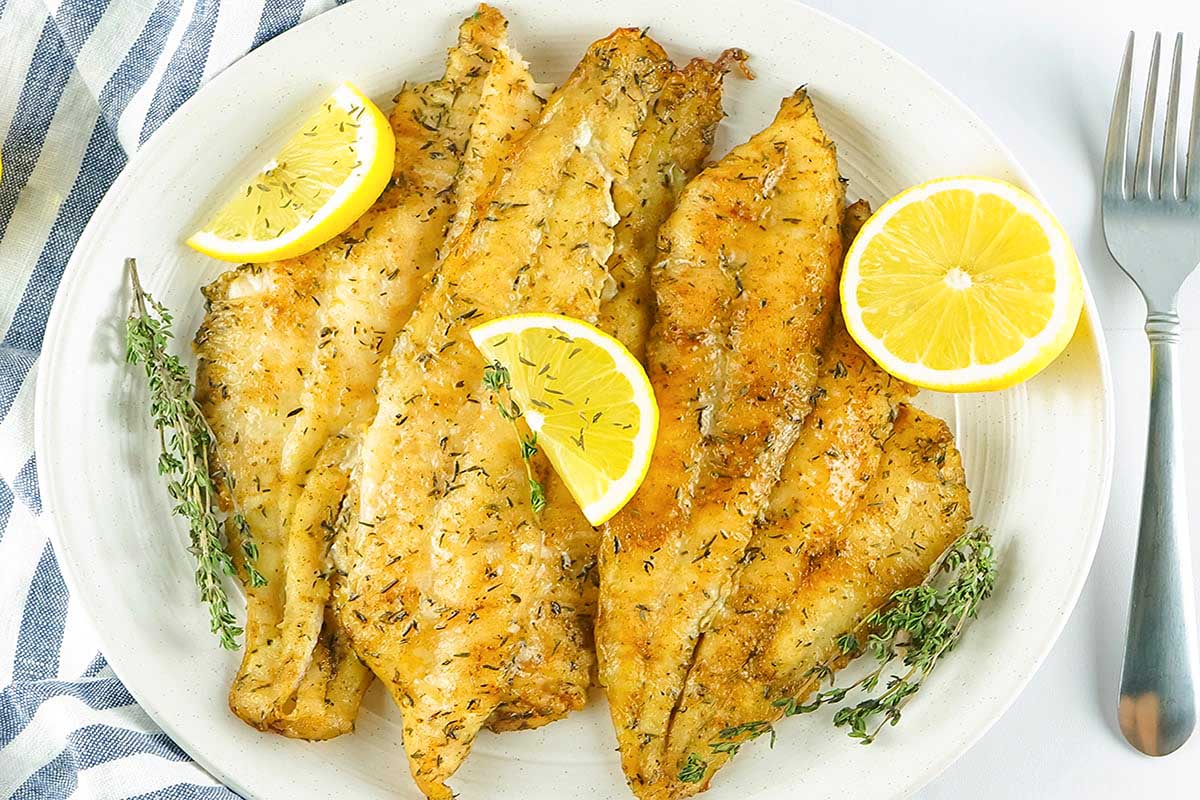 A plate of fried fish with lemon slices.