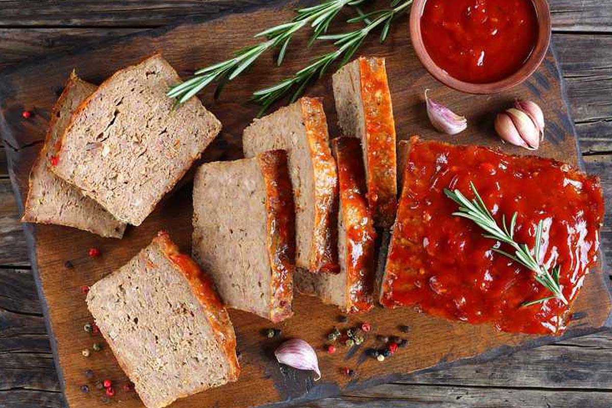 Mouthwatering meatloaf on a rustic wooden cutting board, perfectly complemented by a dollop of ketchup. Explore delightful meatloaf recipes!